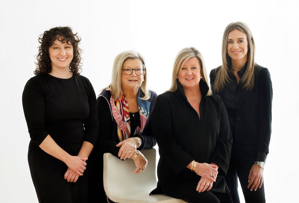 The Conley & Partners real estate team poses for a professional group portrait in a bright studio setting, wearing coordinated black business attire.