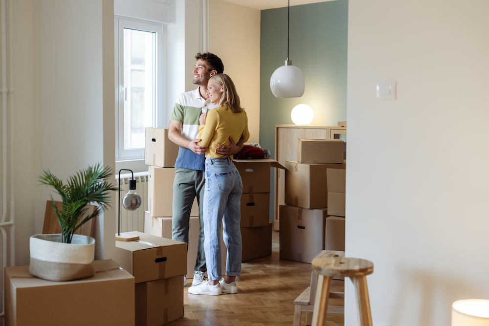 A happy young couple embraces while standing in their new home, surrounded by packed moving boxes, symbolizing new beginnings and the excitement of starting a new chapter in life.