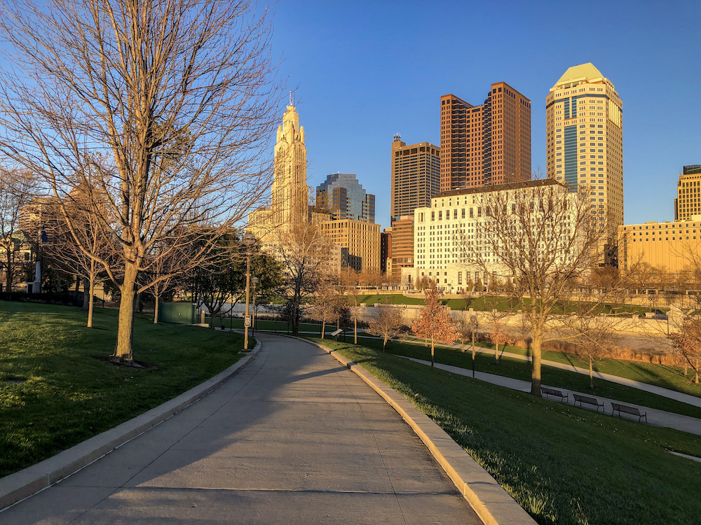 The iconic Columbus Skyline as seen on a stroll through a park. A beautiful blue sky day. Shot in during the blue hour. Copy space in the sidewalk.